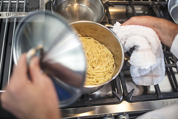 Chefkoch hebt Deckel auf Spaghetti-Pfanne auf dem Herd  Ansicht von oben