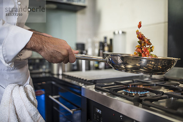 Koch hält Bratpfanne in der Hand  kocht Essen über dem Herd  Nahaufnahme