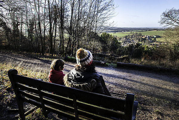 Mutter und Sohn sitzen auf einer Bank in ländlicher Umgebung  Blick auf Ansicht  Rückansicht