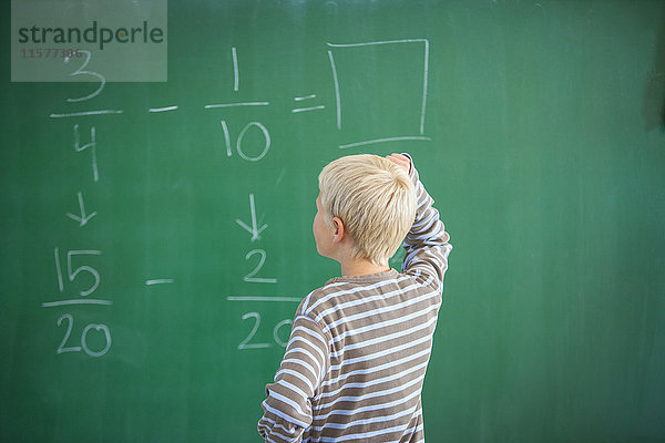 Junge im Klassenzimmer  Ausarbeitung einer Matheaufgabe an der Tafel  Rückansicht