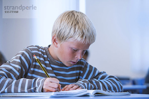 Junge im Klassenzimmer  sitzt am Schreibtisch  macht Klassenarbeiten