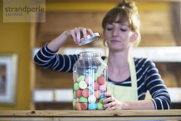 Junge Frau im Lebensmittelgeschäft  öffnet Glas mit Süßigkeiten