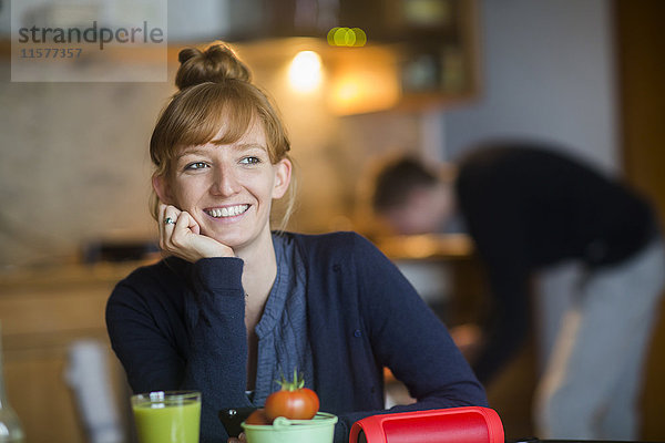 Porträt einer jungen Frau  am Tisch sitzend  Smoothie auf dem Tisch vor ihr