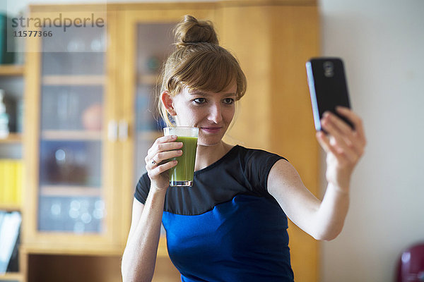 Junge Frau hält Smoothie in der Hand  nimmt Selfie mit Smartphone