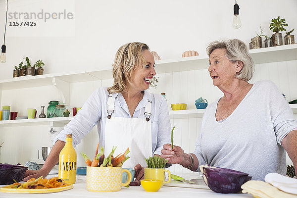 Ältere Frau und Tochter unterhalten sich beim Zubereiten von Gemüse am Küchentisch