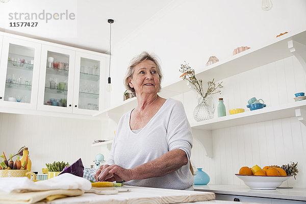 Ältere Frau  die beim Zubereiten von Gemüse am Küchentisch über ihre Schulter schaut