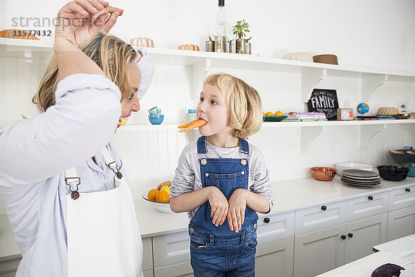 Reife Frau und Tochter imitieren Kaninchen mit Karotten in der Küche
