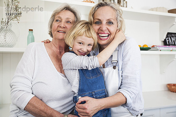 Porträt eines Mädchens  das Mutter und Großmutter in der Küche umarmt