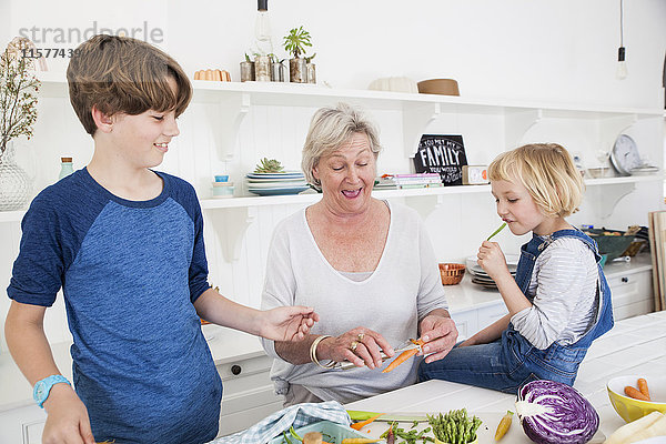 Ältere Frau und Enkelkinder bereiten Gemüse am Küchentisch