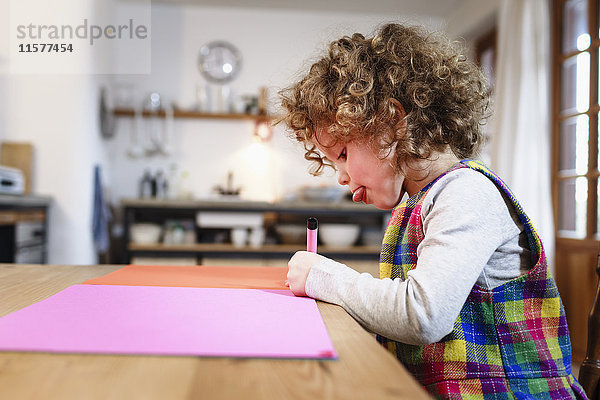 Mädchenzeichnung auf rosa Papier bei Tisch