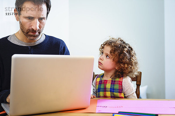 Mädchen starrt Vater an und benutzt Laptop am Tisch