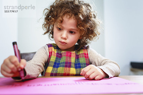 Mädchenzeichnung auf rosa Papier am Tisch