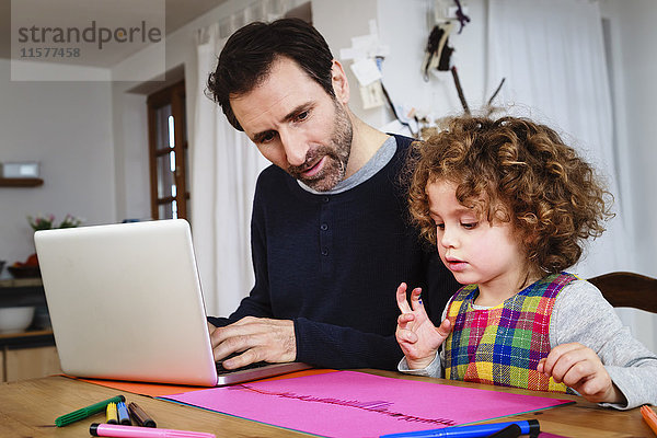 Girl Zeichnung am Tisch  während Vater mit Laptop