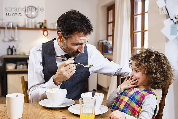 Mann füttert Tochter mit Müsli mit der Hand über dem Mund in der Küche