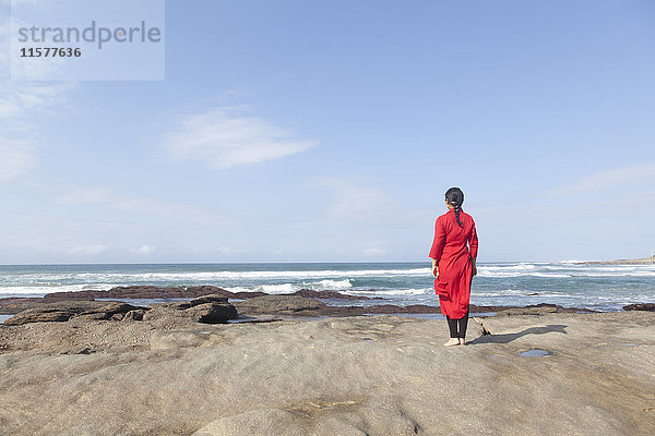 Frau in rotem Kleid  auf Felsen stehend  auf das Meer blickend  Südafrika