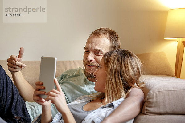 Mittelgroßes erwachsenes Paar entspannt sich auf dem Sofa und schaut auf ein digitales Tablett