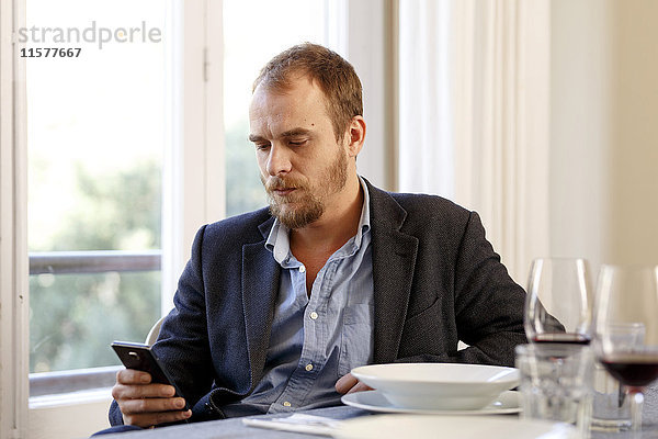 Mann am Esstisch sitzend  mit Smartphone