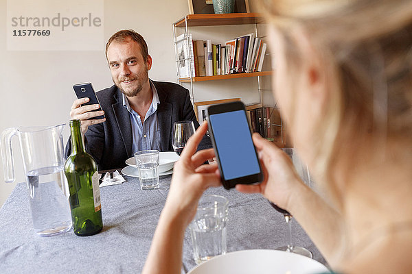 Mittelgroße erwachsene Paare zu Hause  die am Esstisch sitzen und Smartphones benutzen