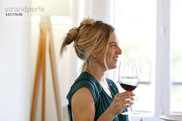 Frau zu Hause  hält ein Glas Wein in der Hand und lächelt