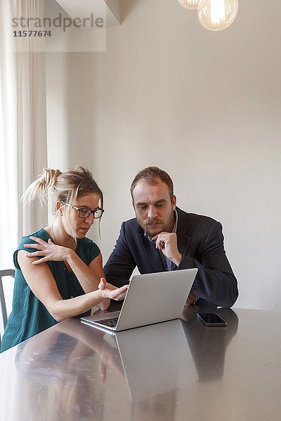 Mittleres erwachsenes Paar sitzt am Tisch und schaut auf den Laptop