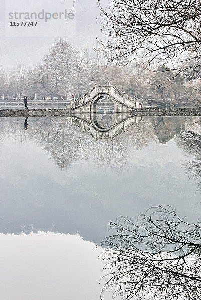 Spiegelbild von kahlen Bäumen und Fußgängerbrücke über den See  Dorf Hongcun  Provinz Anhui  China