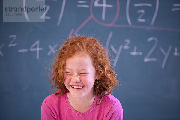 Porträt eines süßen Grundschulmädchens  das im Klassenzimmer kichert