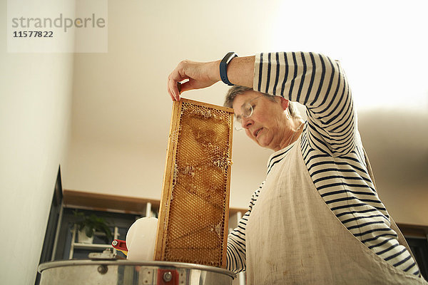 Ältere Imkerin schabt Honigwaben in einen Kochtopf