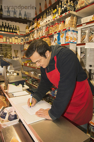 Reifer männlicher Lebensmittelhändler schreibt Notizen im örtlichen italienischen Lebensmittelgeschäft