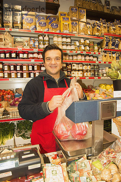 Porträt eines männlichen Lebensmittelhändlers  der in einem italienischen Lebensmittelgeschäft rote Paprika wiegt