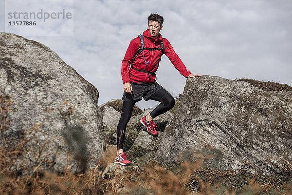 Männlicher Läufer macht eine Pause zwischen Felsblöcken am Stanage Edge  Peak District  Derbyshire  UK