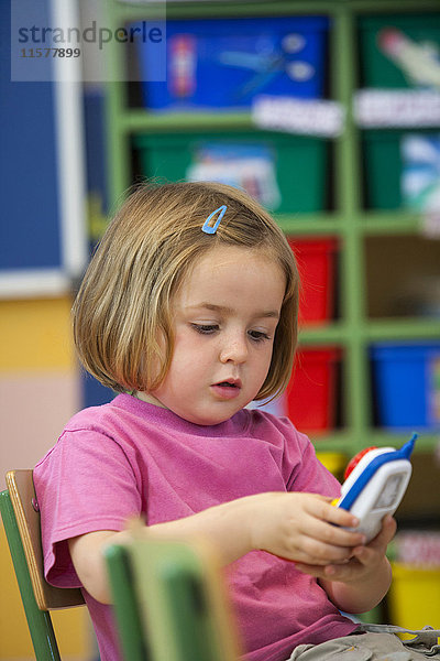 Vorschulmädchen drückt Knöpfe von Spielzeug-Handys im Klassenzimmer