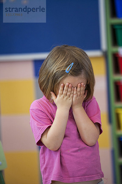 Vorschulmädchen bedeckt im Klassenzimmer ihre Augen mit Händen