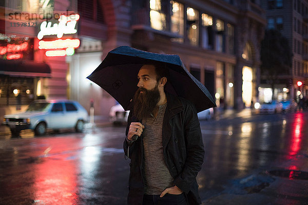 Mittelgroßer erwachsener Mann  der nachts mit einem Regenschirm durch die Stadt läuft  Downtown  San Francisco  Kalifornien  USA