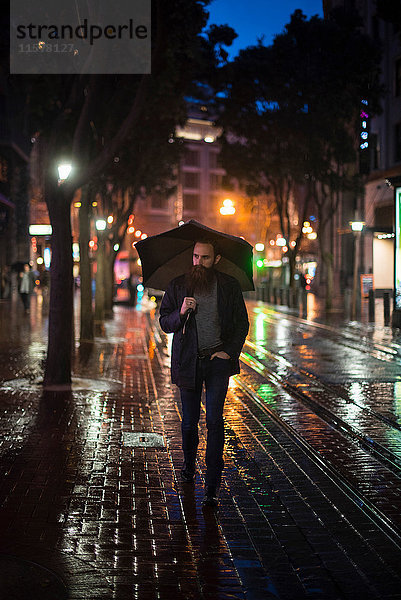 Mittelgroßer erwachsener Mann  der nachts mit einem Regenschirm durch die Stadt läuft  Downtown  San Francisco  Kalifornien  USA