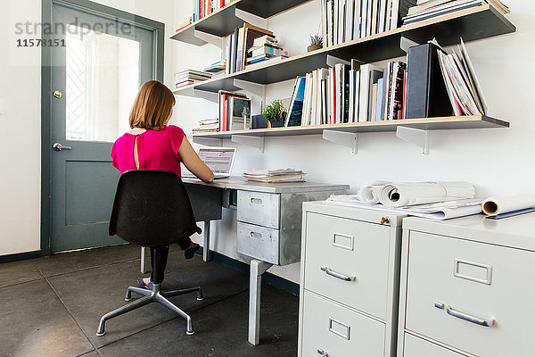Frau sitzt im Büro am Schreibtisch und arbeitet am Laptop