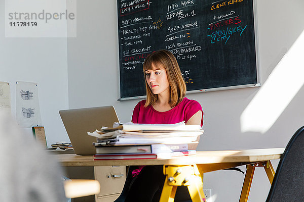 Frau sitzt im Büro am Schreibtisch und arbeitet am Laptop