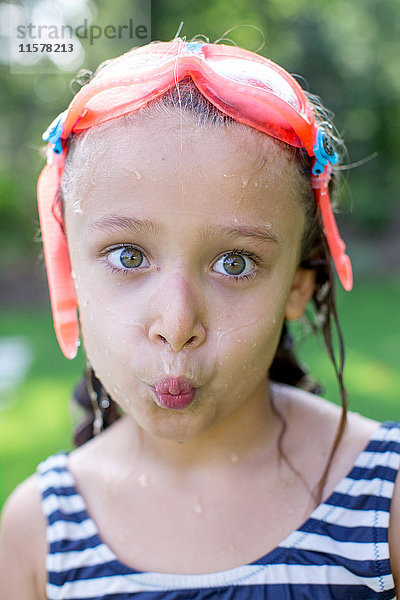 Porträt eines Mädchens mit Schwimmbrille und kräuselnden Lippen im Garten