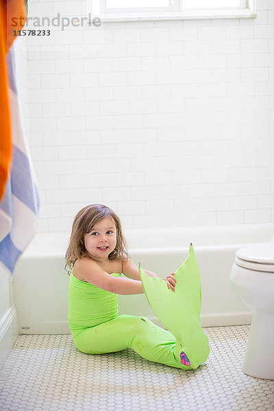 Porträt eines Mädchens in lindgrünem Meerjungfrauenkostüm  das auf dem Badezimmerboden sitzt