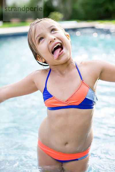 Mädchen steht im Freibad und streckt die Zunge heraus