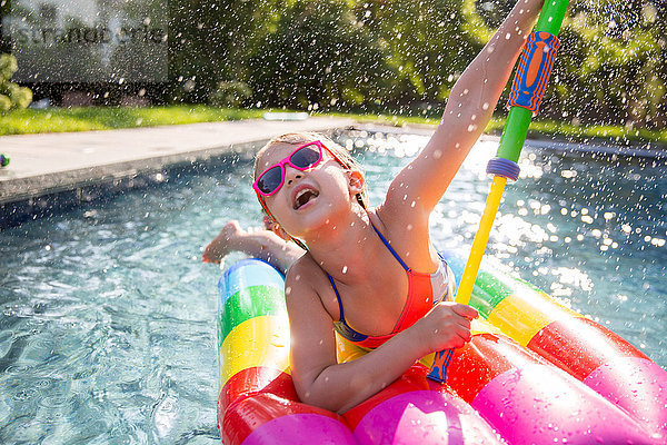 Mädchen im Bikini beim aufblasbaren Spielen mit Wasserpistole im Freibad