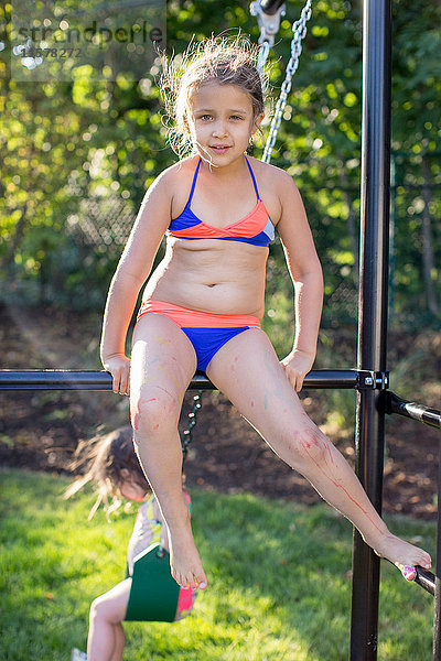Porträt eines Mädchens im Bikini  das auf einem Klettergerüst im Garten sitzt