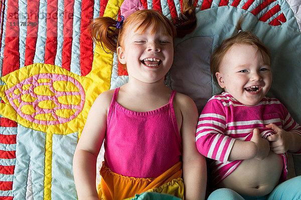Porträt von zwei jungen Schwestern  die lachend auf einer Decke liegen