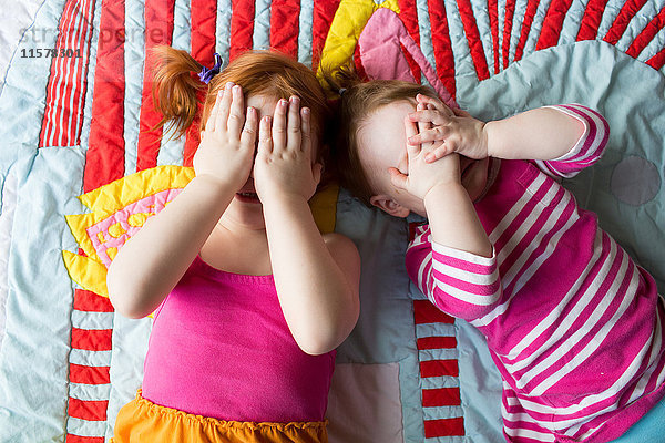 Porträt von zwei jungen Schwestern  die auf einer Decke liegen und das Gesicht mit den Händen bedecken