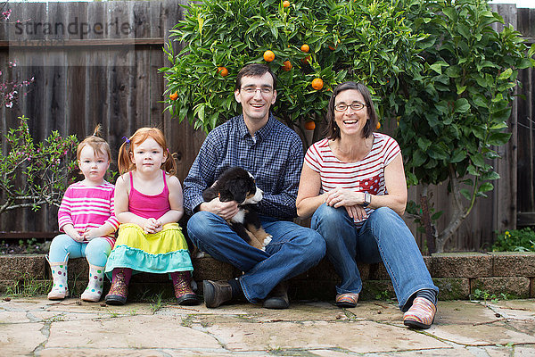 Porträt einer jungen Familie mit Hund  im Garten sitzend