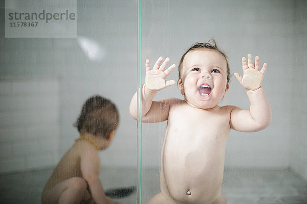 Nacktes Kleinkind lehnt in Dusche gegen Glastür