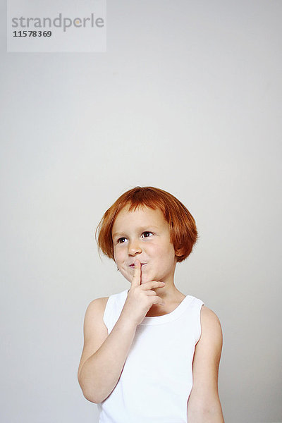 Porträt eines rothaarigen Mädchens im Haus  das seinen Finger vor den Mund hält  mit einem fragenden Gesichtsausdruck.