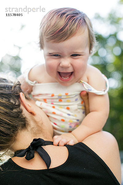 Über-Schulter-Ansicht einer Frau  die ein Kleinkind im Garten hochhält
