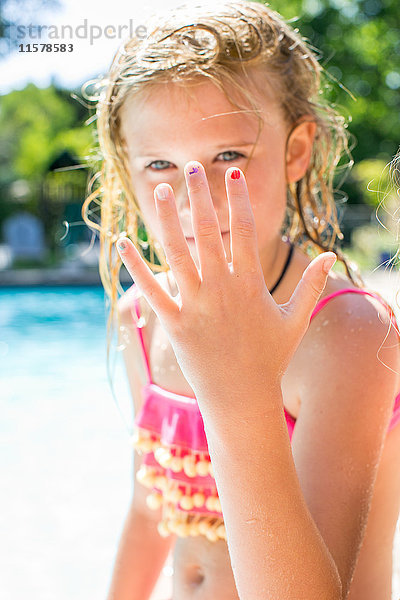 Porträt eines Mädchens mit erhobener Hand am Swimmingpool