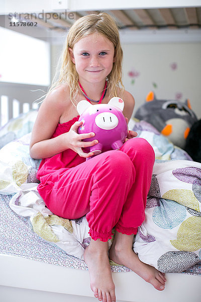 Porträt eines Mädchens  das auf einem Etagenbett sitzt und ein Sparschwein hält