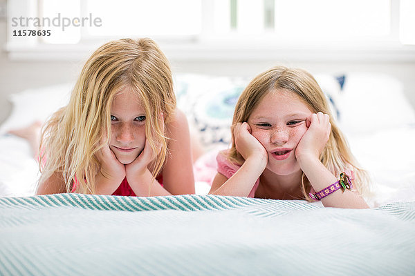 Porträt eines Mädchens und einer Schwester  die im Bett Gesichter ziehen